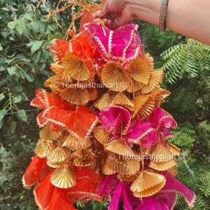 May include: A bunch of decorative hanging tassels in orange, pink, and gold. The tassels are made of fabric and have a metallic gold finish. They are tied together with a string and are ready to be hung.