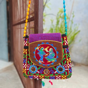May include: A colorful embroidered crossbody bag with a red velvet flap featuring a dancing couple. The bag has a beaded strap and a variety of colorful floral and geometric patterns.