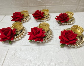 Puede incluir: Seis candelabros dorados con adornos de rosas rojas y detalles de perlas. Los candelabros están dispuestos en círculo sobre una superficie blanca.