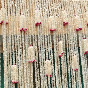 Op de afbeelding: Een decoratief achtergrond met verticale strengen van off-white, getextureerd materiaal, versierd met clusters van kleine, helder roze accenten. De strengen cre&euml;ren een gelaagd effect. De algehele esthetiek is zacht en elegant, geschikt voor evenementen of interieurdecoratie.