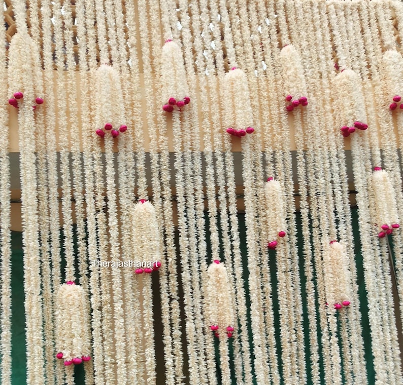 Op de afbeelding: Een decoratief achtergrond met verticale strengen van off-white, getextureerd materiaal, versierd met clusters van kleine, helder roze accenten. De strengen cre&euml;ren een gelaagd effect. De algehele esthetiek is zacht en elegant, geschikt voor evenementen of interieurdecoratie.