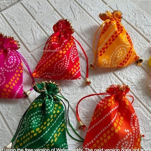 Op de afbeelding: Vijf kleine trekkoordtassen gemaakt van kleurrijk stof met een wit en geel patroon. De tassen zijn vastgebonden met een touwtje en hebben een kleine bel aan het uiteinde van het touwtje.