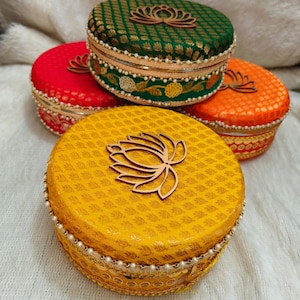 Puede incluir: Cuatro cajas redondas decorativas con un diseño de flor de loto. Las cajas son en tonos de verde, rojo, naranja y amarillo. Cada caja tiene un borde dorado y un borde de perlas.