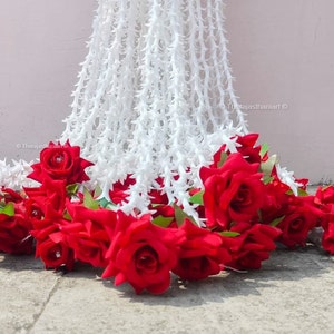 May include: A white garland with a thorny design is draped over a wall. A cluster of red roses are placed at the bottom of the garland.