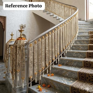 May include: A curved staircase with marble steps and a decorative metal balustrade. The balustrade features gold detailing and hanging beaded decorations. Scattered orange flowers add a touch of colour.