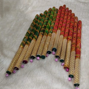 May include: A set of colorful wooden sticks with gold trim and pink bells. The sticks are decorated with a variety of patterns, including stripes, polka dots, and floral designs.