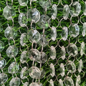 May include: Close-up of a decorative crystal curtain. The clear, faceted crystals are linked together with silver-colored rings. The background is a vibrant green, creating a striking contrast. The crystals are in various shapes and sizes.