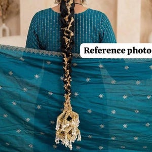May include: A long, black braid adorned with gold embellishments and white pearls. The braid is attached to a teal-colored garment with gold detailing. The image is labeled "Reference photo".