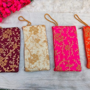 Könnte beinhalten: Vier bestickte Beutel mit goldfarbenem Garn auf verschiedenen Stoffen. Die Beutel sind burgunderrot, cremefarben, rosa und orange. Jeder Beutel hat einen goldenen Kordelgriff.