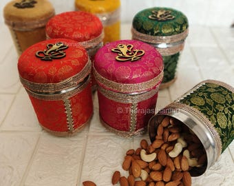 May include: A set of six decorative metal containers with lids. The containers are covered in colorful fabric with intricate patterns. The lids feature a gold-colored design. The containers are filled with almonds and cashews.