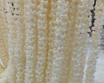 May include: Close-up of multiple strands of off-white, flower-shaped garlands. The garlands are densely packed, creating a textured, layered effect. The flowers are small and clustered, with a delicate, almost translucent appearance.