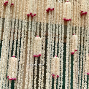 Op de afbeelding: Een decoratieve achtergrond met talrijke strengen cr&egrave;mekleurig, getextureerd materiaal, versierd met clusters van kleine, felroze accenten. Het ontwerp cre&euml;ert een gelaagd effect, geschikt voor evenementdecoratie.