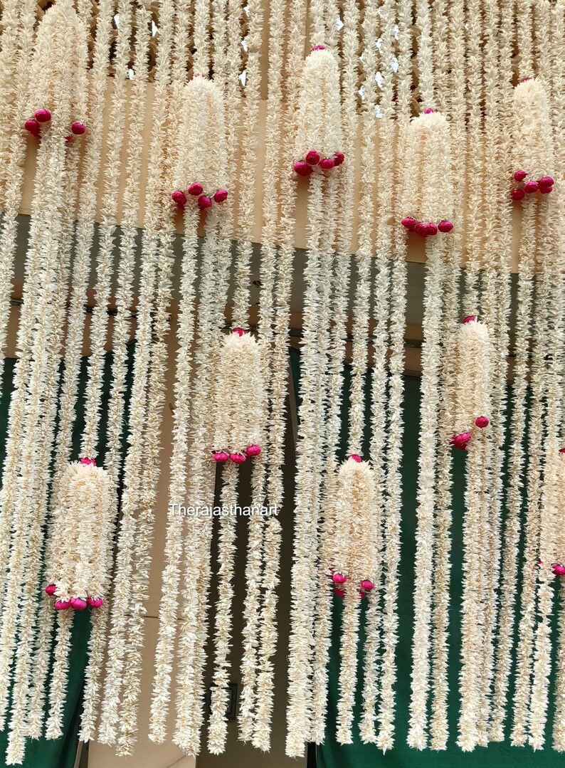 Op de afbeelding: Een decoratieve achtergrond met talrijke strengen cr&egrave;mekleurig, getextureerd materiaal, versierd met clusters van kleine, felroze accenten. Het ontwerp cre&euml;ert een gelaagd effect, geschikt voor evenementdecoratie.