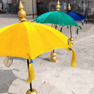 K&ouml;nnte beinhalten: Drei dekorative Regenschirme mit goldenen Spitzen und Quasten. Die Regenschirme sind gelb, gr&uuml;n und blau. Die Regenschirme stehen auf St&auml;ndern mit goldenen Sockeln.