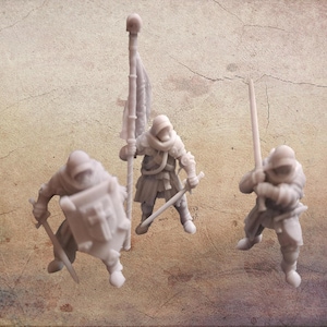 May include: Three miniature figurines of medieval knights in armor. One knight holds a banner, another a shield, and the third a sword. The figures are a light gray color and stand on a textured, tan surface.