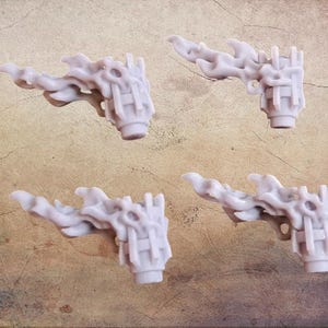 Puede incluir: Cuatro esculturas en miniatura con forma de llama, de color gris claro. Cada pieza tiene un diseño texturizado y detallado con una base cilíndrica. Las esculturas están dispuestas sobre una superficie texturizada y beige. Parecen componentes para un proyecto más grande.