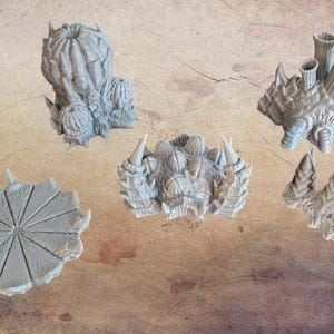 May include: A collection of gray, textured, fantasy-themed miniature terrain pieces. The set includes various organic shapes, such as spiky formations and a segmented, circular base, suitable for tabletop gaming.