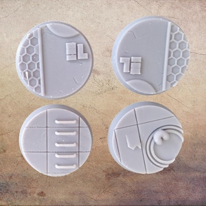 Puede incluir: Cuatro bases redondas de plástico gris con diferentes diseños. Las bases son para juegos de guerra en miniatura.