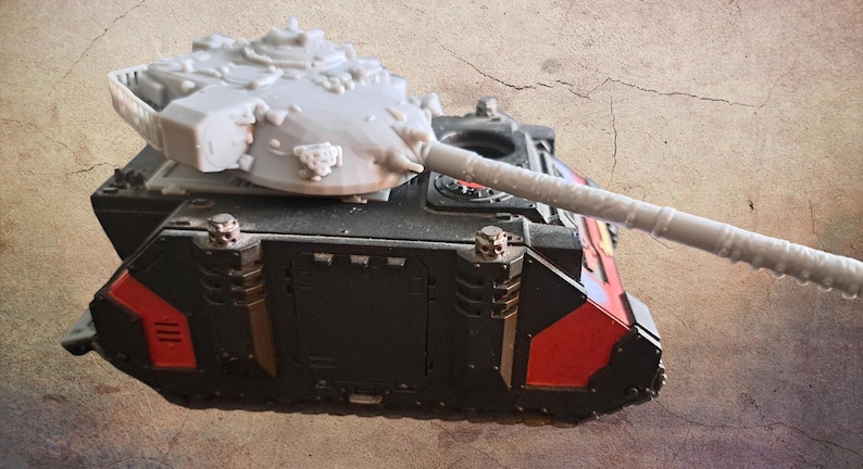 May include: A miniature tank model featuring a black and red chassis with metallic accents and a light gray, unpainted turret with a long barrel. The vehicle has a boxy, armored design with visible mechanical details and small skull-shaped ornaments.