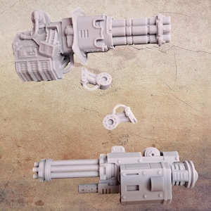 May include: Three unpainted grey miniature gun models, possibly for a hobby or gaming project. The image shows two large guns with multiple barrels and a smaller detached component. The models are likely made of plastic.