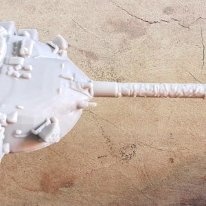 May include: A light gray, unpainted resin model of a tank turret featuring a long, cylindrical main gun barrel, a circular hatch, various small mechanical details, and a rear storage rack, captured from a top-down perspective.