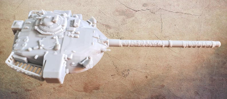 May include: A light gray, unpainted resin model of a tank turret featuring a long, cylindrical main gun barrel, a circular hatch, various small mechanical details, and a rear storage rack, captured from a top-down perspective.