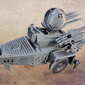 May include: A grey 3D-printed scale model of a mobile air defence system featuring a tapered chassis, a central turret with a spherical sensor housing, and two side-mounted launchers each holding three long, pointed missiles on a single rubber tyre.