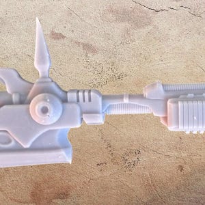Peut inclure: Une arme de science-fiction en plastique blanc avec une lame, une poignée et un long canon. L'arme présente des détails complexes et un design futuriste.