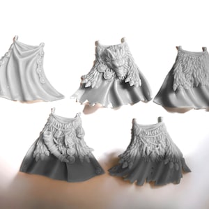 Könnte beinhalten: Fünf graue Fantasy-Umhänge mit unterschiedlichen Designs. Ein Umhang hat dekorative Kreise, während andere Fell, Federn und Hörner aufweisen. Die Umhänge sind wahrscheinlich für Miniaturfiguren oder Cosplay gedacht.