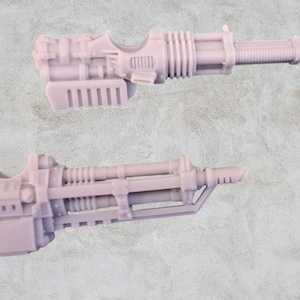 Op de afbeelding: Twee ongeverfde plastic modelgeweren, een met een lange loop en de andere met een kortere loop. Beide geweren hebben een gedetailleerd ontwerp met meerdere onderdelen.