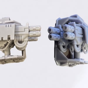 May include: Two grey plastic model guns with multiple barrels and a base. The guns are in a side-by-side view.