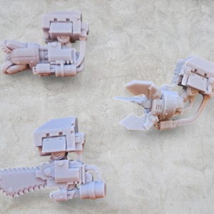 Puede incluir: Tres accesorios de brazo de robot impresos en 3D. Uno es una garra, otro es un taladro y el último es una sierra.