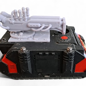 May include: A black and red tank with a grey, detailed, multi-barreled weapon mounted on top. The weapon has a circular base and multiple pipes and tubes.