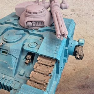 May include: A detailed model of a light blue military tank with a large gun turret and multiple barrels. The tank has a textured surface and dark grey tracks. The turret is a light grey colour.
