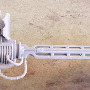 May include: A light grey, futuristic weapon with a blade-like end and various mechanical components. The design includes a series of rectangular cutouts along the blade and a complex arrangement of tubes and housings.