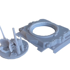 Puede incluir: Un kit de maqueta de torreta de tanque de plástico gris con un conjunto de cañón separado. La torreta es de forma cuadrada con una abertura circular para el cañón. El conjunto del cañón tiene varios cañones y un escudo.