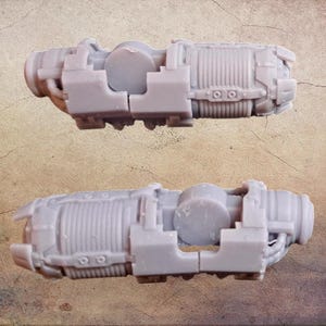 Puede incluir: Se muestran dos modelos de motor en miniatura de color gris. Cada modelo tiene un cuerpo cilíndrico con detalles acanalados, un componente circular central y varias partes salientes. Los modelos son probablemente para aficionados o modelistas.