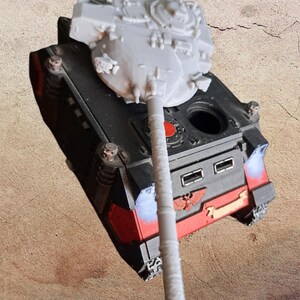 May include: A miniature tank model featuring a black and red chassis with a prominent red eagle emblem on the front. The tank has a long, light gray turret barrel and a light gray turret top, with a small circular red detail on the upper deck.