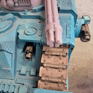 Könnte beinhalten: Nahaufnahme eines Modellpanzers, hauptsächlich in Blau- und Grautönen. Der Panzer verfügt über ein Mehrfachlauf-Geschütz, eine detaillierte Kette und verschiedene mechanische Komponenten. Das Modell ist eine Miniaturreplik, die komplizierte Designelemente zeigt.