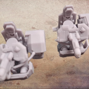 Könnte beinhalten: Zwei unbemalte, hellgraue Miniaturmodellkomponenten. Jede Komponente weist ein komplexes Design mit einem Sitz, einer großen rechteckigen Struktur und verschiedenen mechanischen Details auf. Die Modelle sind wahrscheinlich für ein Tabletop-Spiel oder Hobby gedacht.