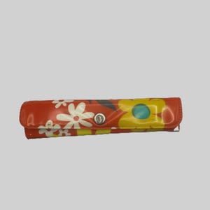 May include: A red, rectangular case with a floral pattern of white and yellow flowers. The case has a silver snap closure and a curved top. The case is likely for eyeglasses or sunglasses.