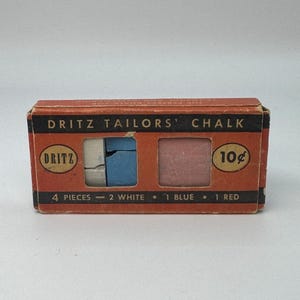 May include: A vintage box of Dritz Tailors' Chalk, featuring four pieces: two white, one blue, and one red. The orange box has the brand name and price printed on it. The chalk is used for marking fabric.