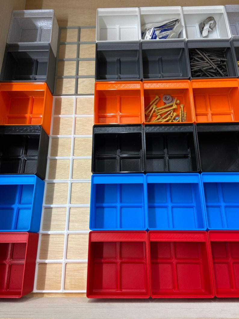 May include: A drawer organizer system featuring a variety of colorful, small, open-top storage bins. The bins are in shades of gray, orange, black, blue, and red. Some bins contain screws and other small hardware. The organizer is set in a wooden drawer.