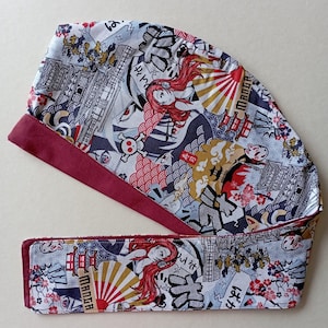 May include: A red and white patterned fabric with Japanese characters and images of a pagoda, a sun, and a woman with red hair. The fabric has a burgundy trim.