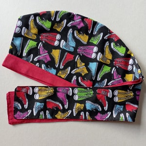 May include: A red and black fabric scrub hat with a colorful pattern of sneakers. The hat has a tie that wraps around the back of the head.