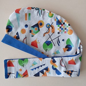 May include: A white fabric scrub hat with a blue trim and a geometric pattern in shades of orange, green, blue, and black. The pattern features circles, squares, and triangles.
