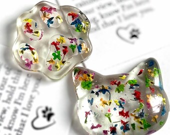 May include: Two clear resin cat-themed accessories, one paw-shaped and one cat-head shaped, each filled with colorful dried flowers. The paw measures approximately 1.5 inches across. The cat head measures approximately 1.25 inches across.
