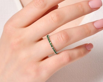 Puede incluir: Un delicado anillo de eternidad con una fila de pequeñas piedras preciosas de color verde esmeralda engastadas en una banda de plata.