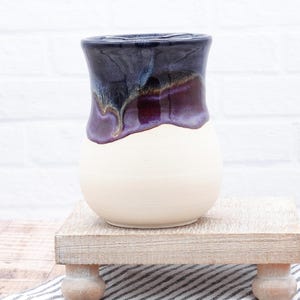 May include: A white ceramic vase with a dark purple and blue glaze. The glaze has a drip effect and creates a unique pattern.