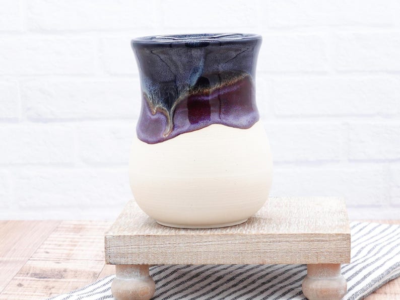 May include: A white ceramic vase with a dark purple and blue glaze. The glaze has a drip effect and creates a unique pattern.